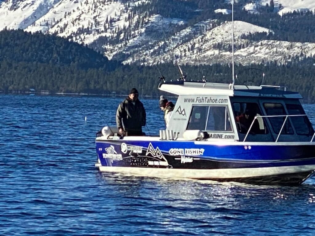 Lake Tahoe fishing charter boat “Gone Fishin” on the water with snowy mountains in the background