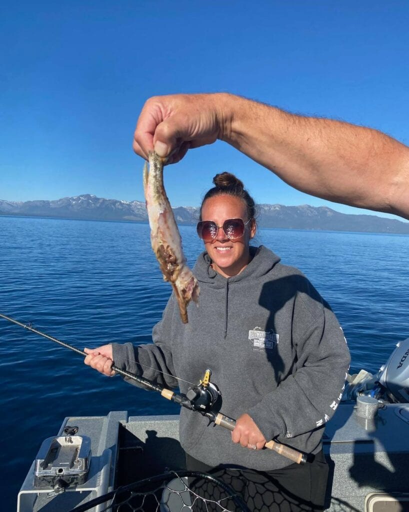 Woman holding fishing rod while friend shows chewed-up baitfish on Lake Tahoe