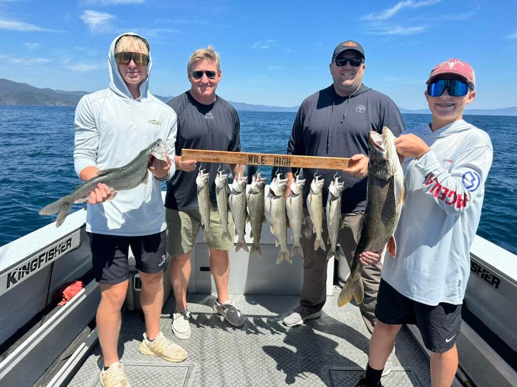 Family group holding Lake Trout on Lake Tahoe fishing trip with snow-capped mountains