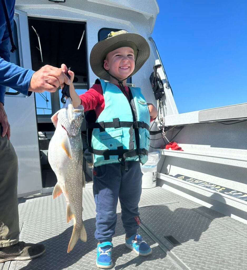 Young boy smiling with large Lake Trout aboard Tahoe fishing charter