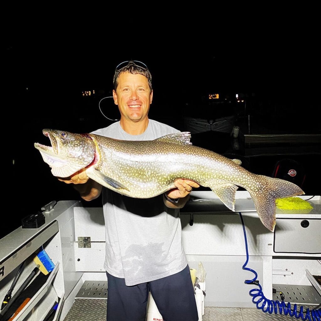 Angler holding trophy-size Lake Trout at night on Lake Tahoe charter boat