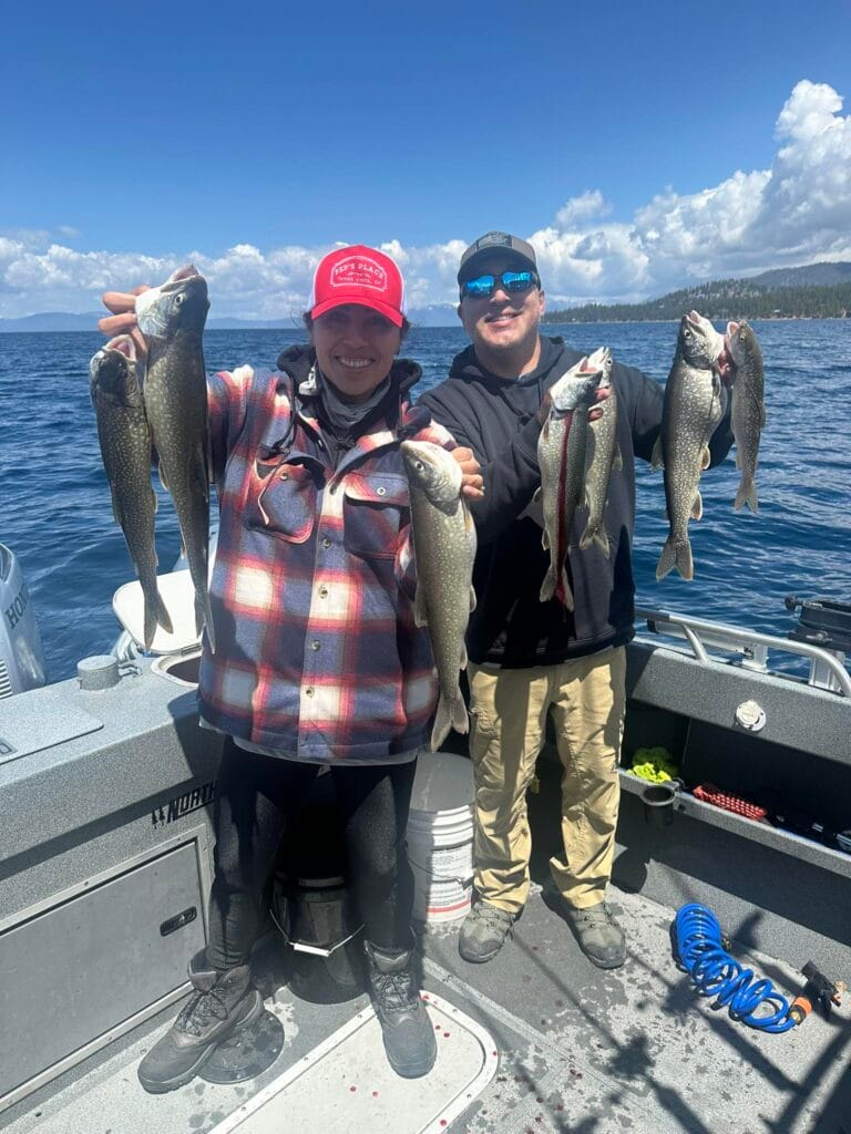 Smiling couple showing off Lake Trout catches on Lake Tahoe fishing charter